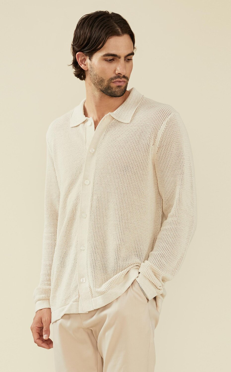 Man wearing an ivory open knit button up sweater and cream trousers