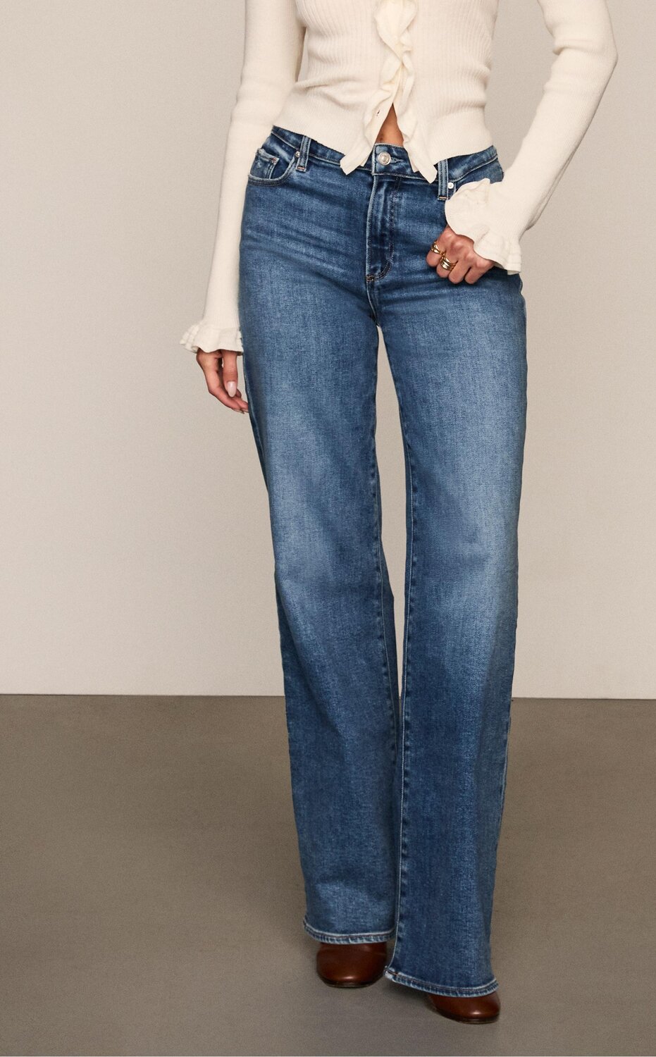 Woman wearing a white knit cardigan, medium blue wash jeans, and brown leather shoes