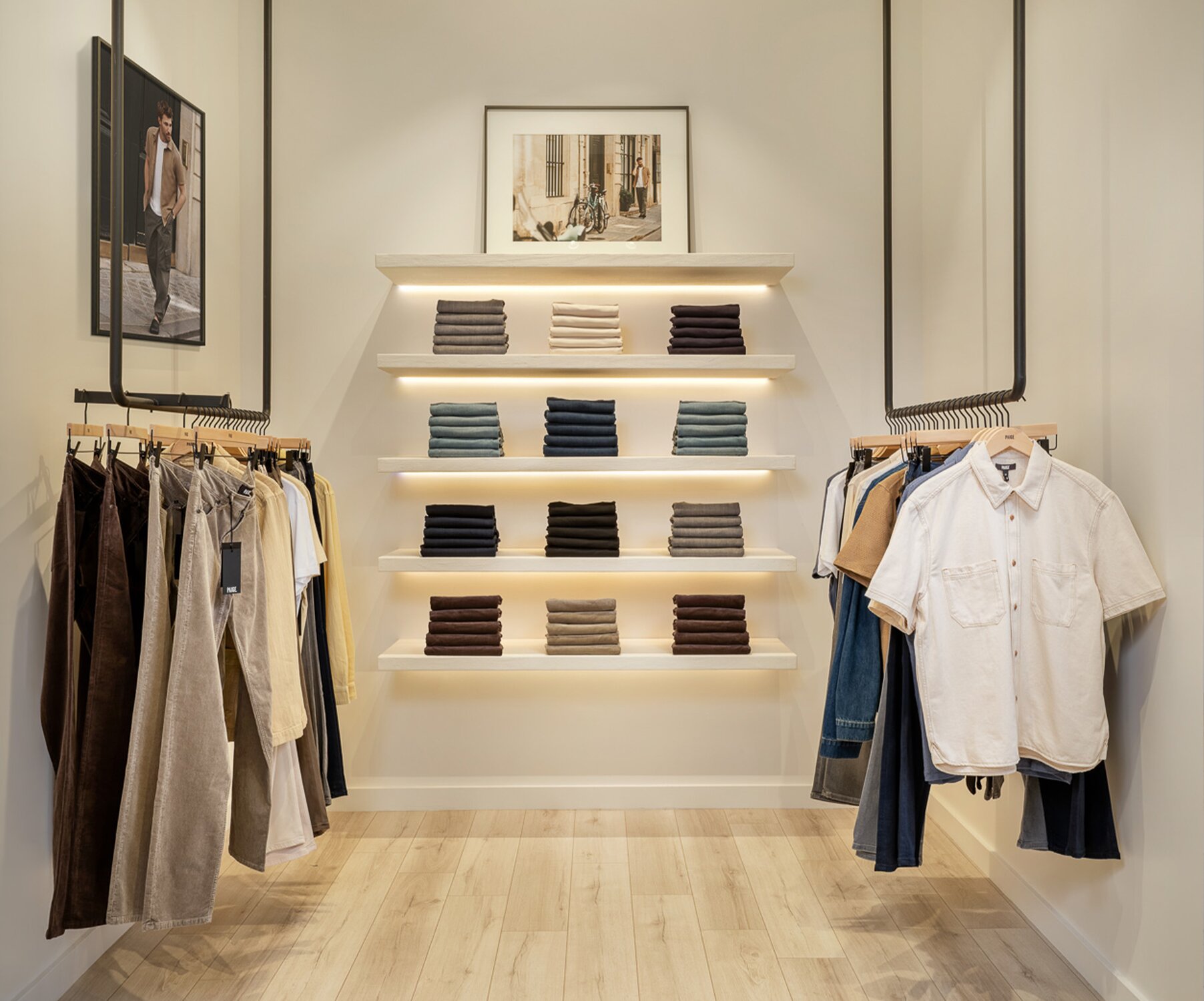 Interior of a PAIGE retail store featuring men's clothing racks, folded denim, and modern minimalist displays.