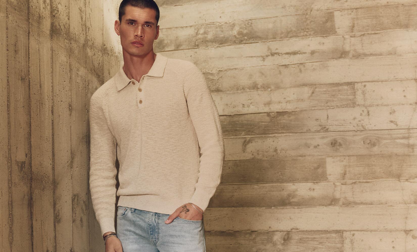 Man wearing a cream long sleeve sweater polo, light wash jeans, and slate grey boots
