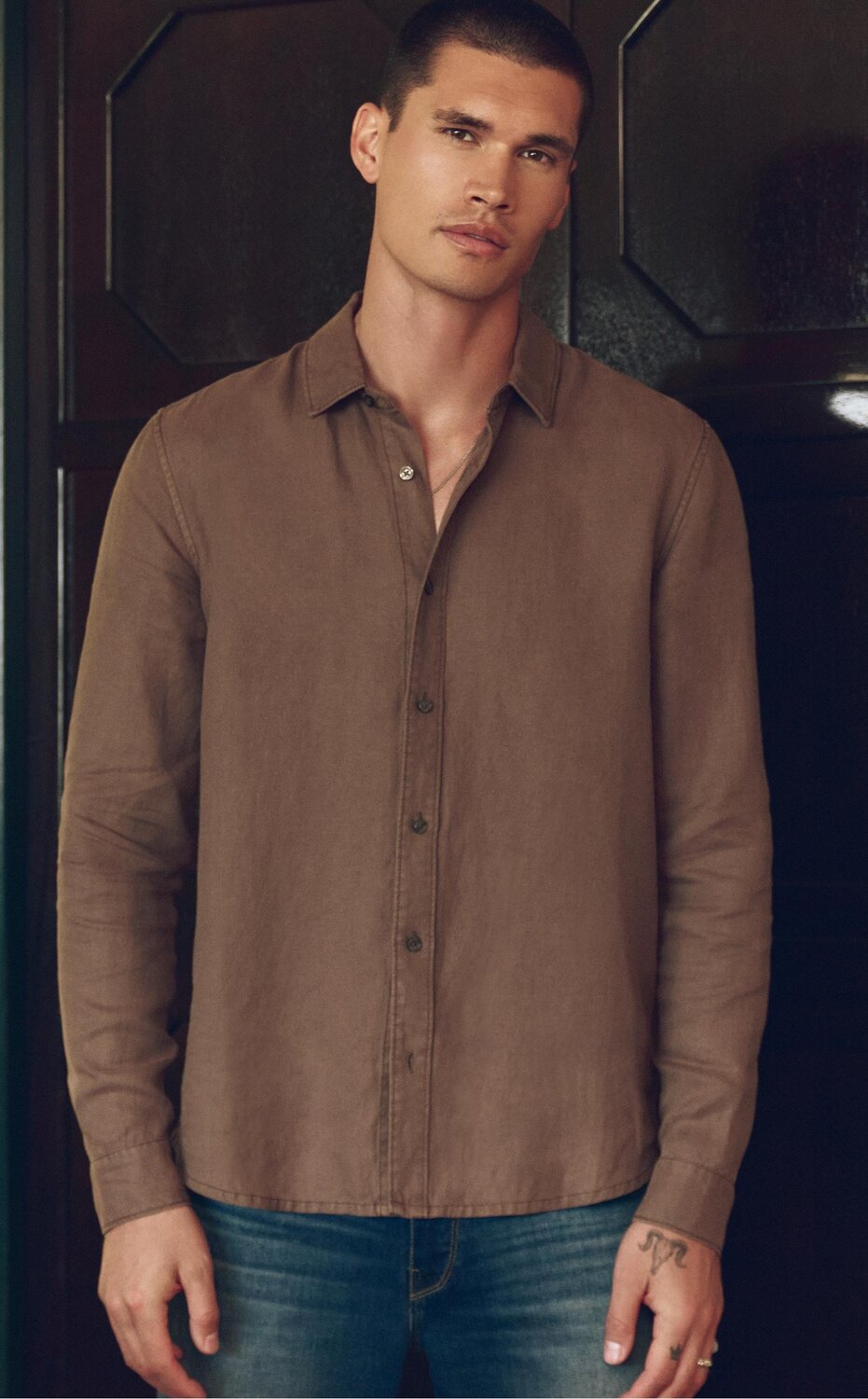 Man wearing a brown long sleeve button up shirt and dark wash jeans
