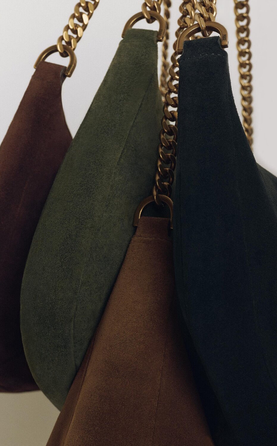 A detail shot of the new handbag collection featuring brown, birch, tobacco and black suede with gold metal hardware and chain detail.