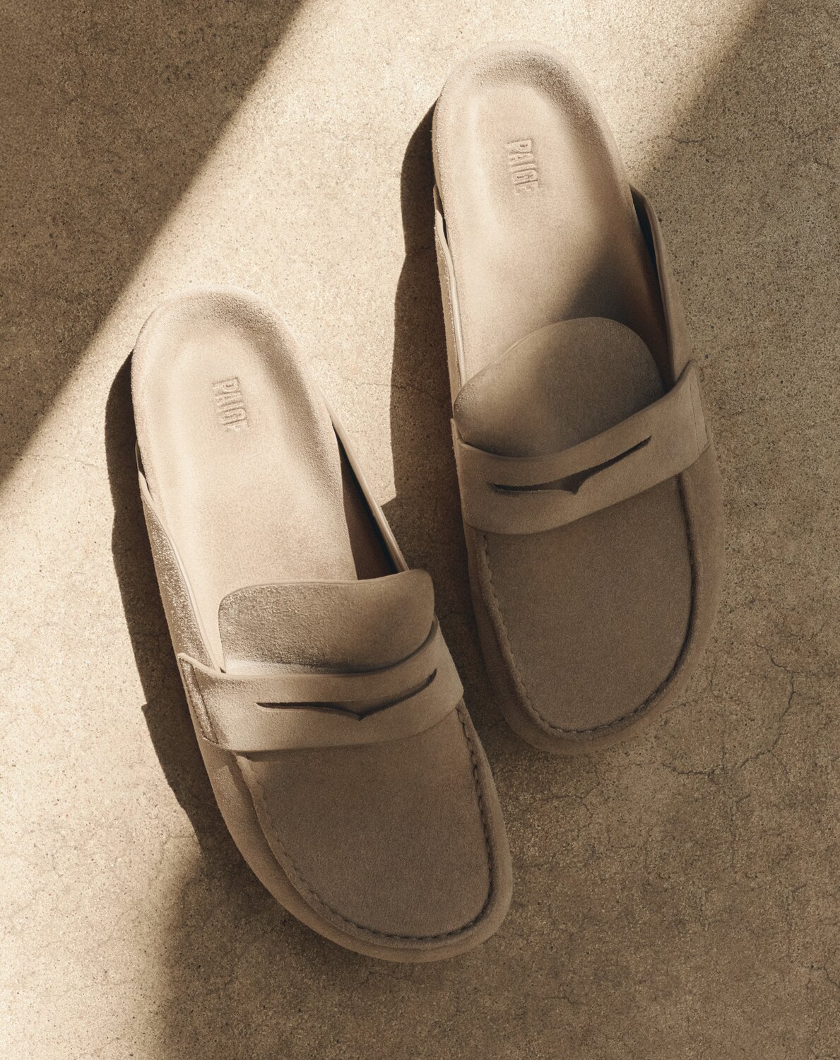 Pair of tan suede slip-on loafers, placed on sunlit stone steps.