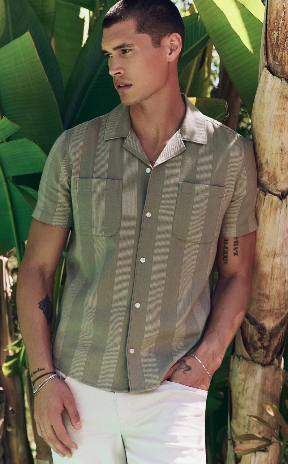 Man wearing a green vertical striped short sleeve shirt with ivory straight leg jeans