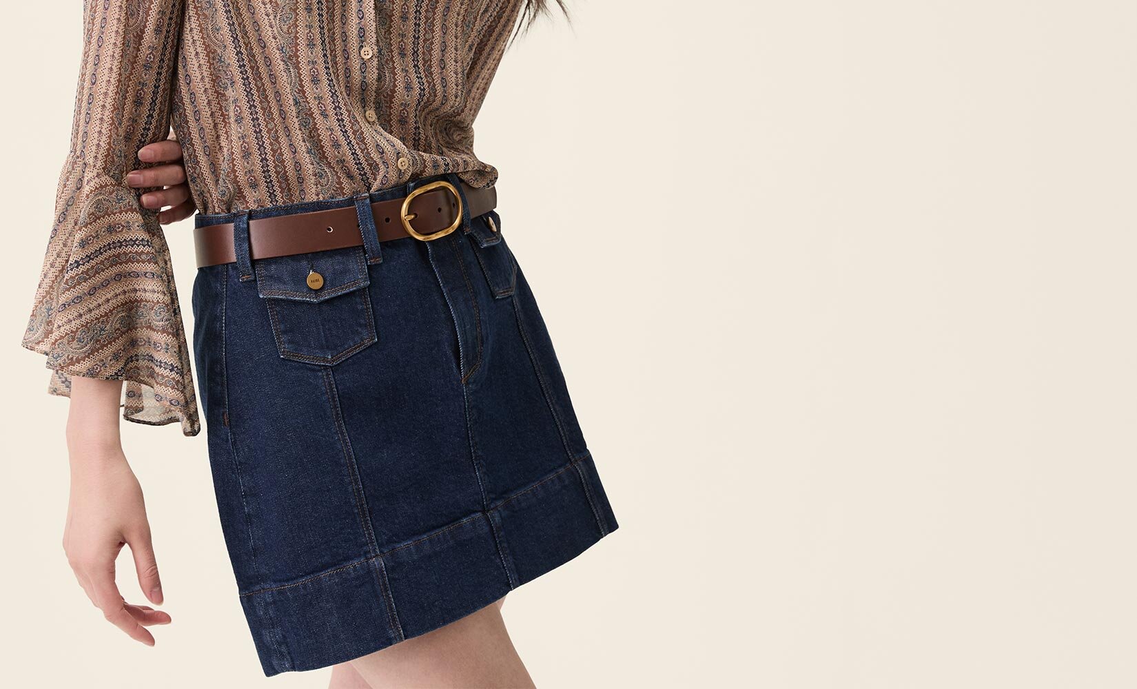 Woman wearing a brown paisley printed blouse, dark wash mini skirt, and brown belt