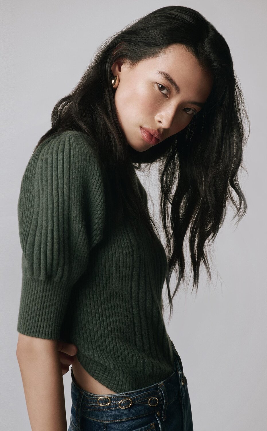 Woman wearing a green puff sleeve sweater top with dark wash wide leg jeans and auburn boots