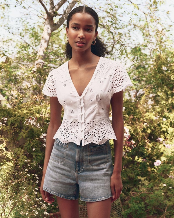 Woman wearing a white short sleeve button up blouse and light wash denim shorts