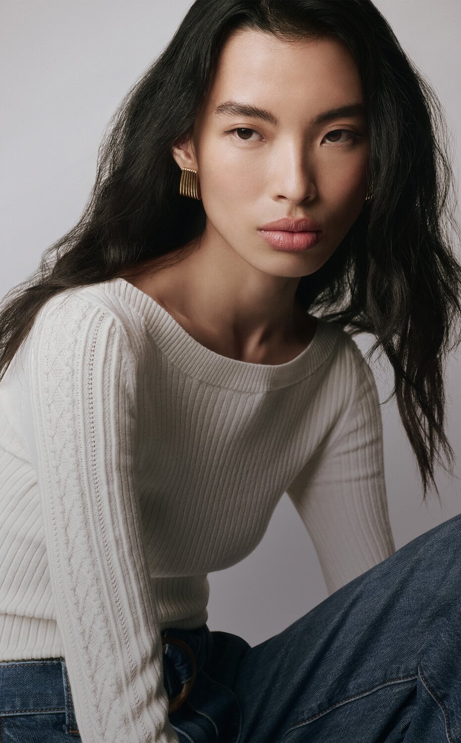 Woman wearing an ivory sweater with belted medium wash wide leg jeans