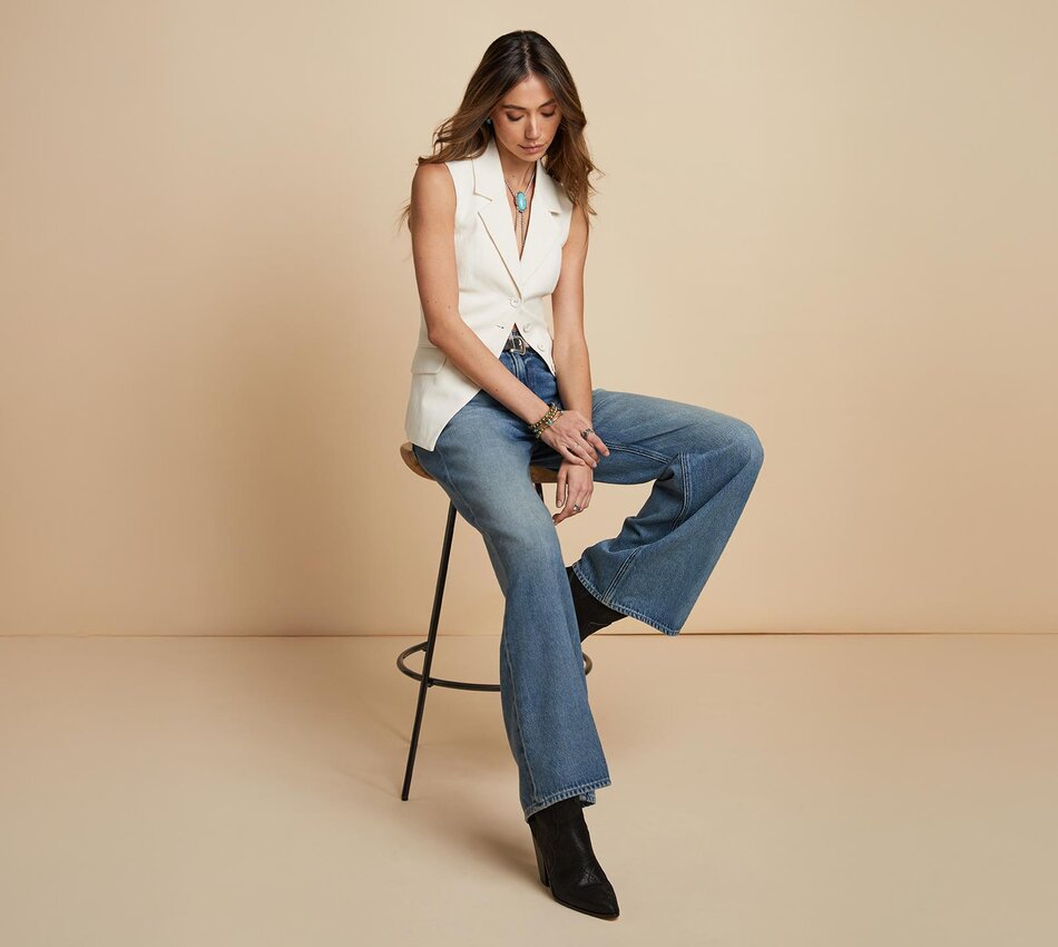 Woman standing a light blue quilted jacket, white tee, medium wash jeans and bone ankle boots