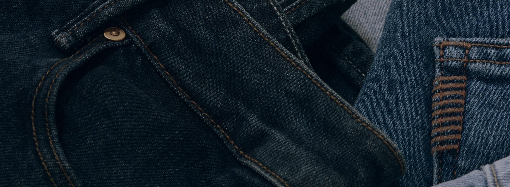 Close-up of stacked denim in varied blue washes, highlighting pocket, rivet, and back-pocket details.