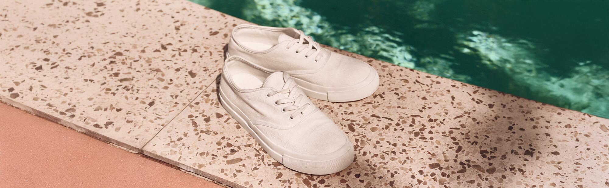 A pair of white canvas sneakers by the pool