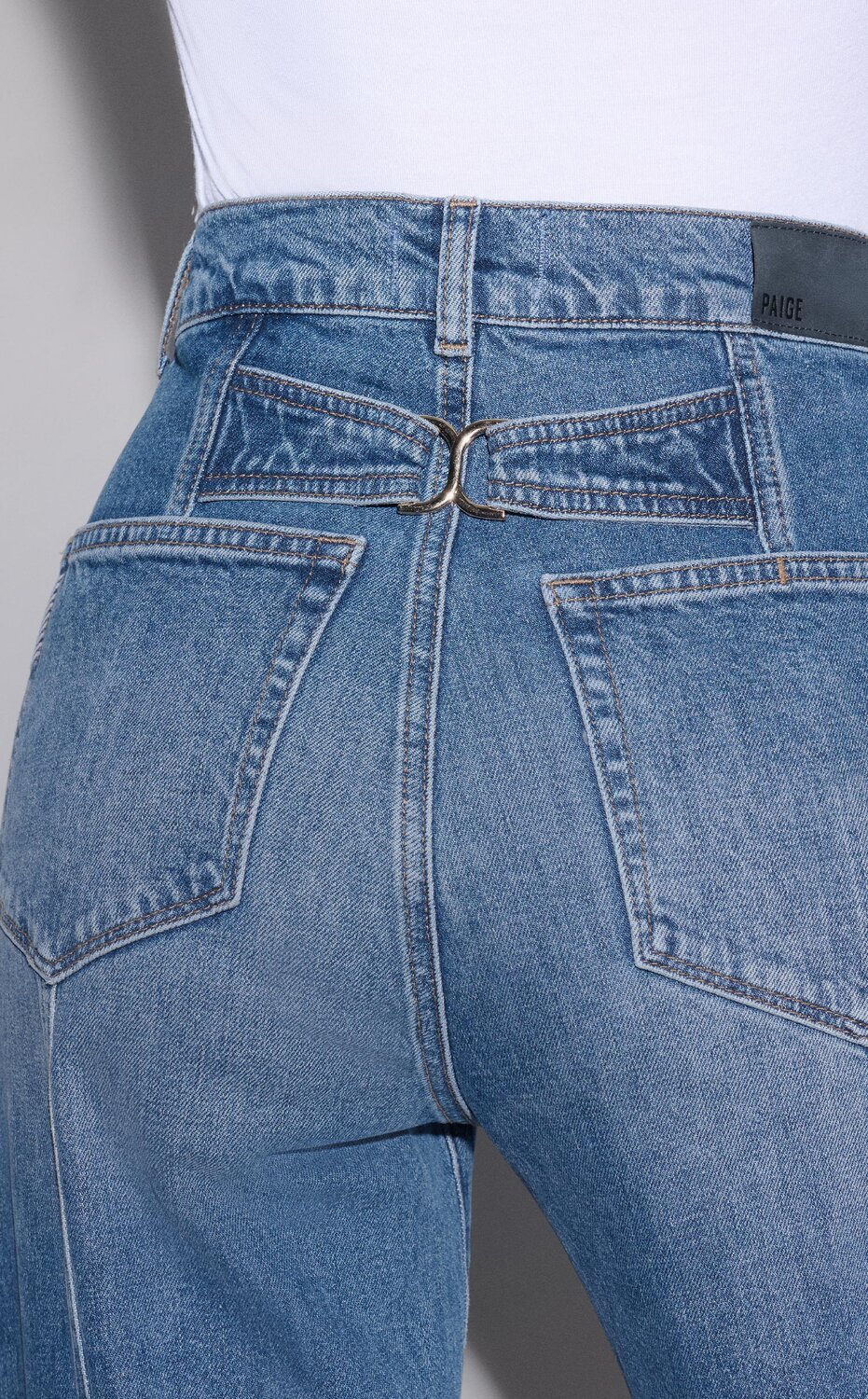 Woman wearing a pair of light wash barrel leg jeans with back seams and a back silver hardware detail