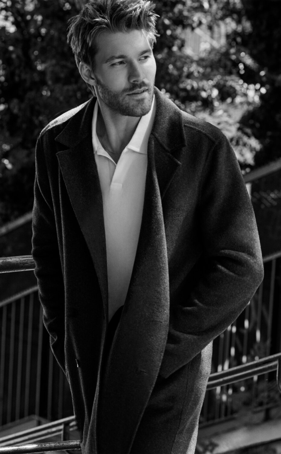Male model wearing a dark tailored coat layered over a light sweater and trousers from the PAIGE men's fall collection.