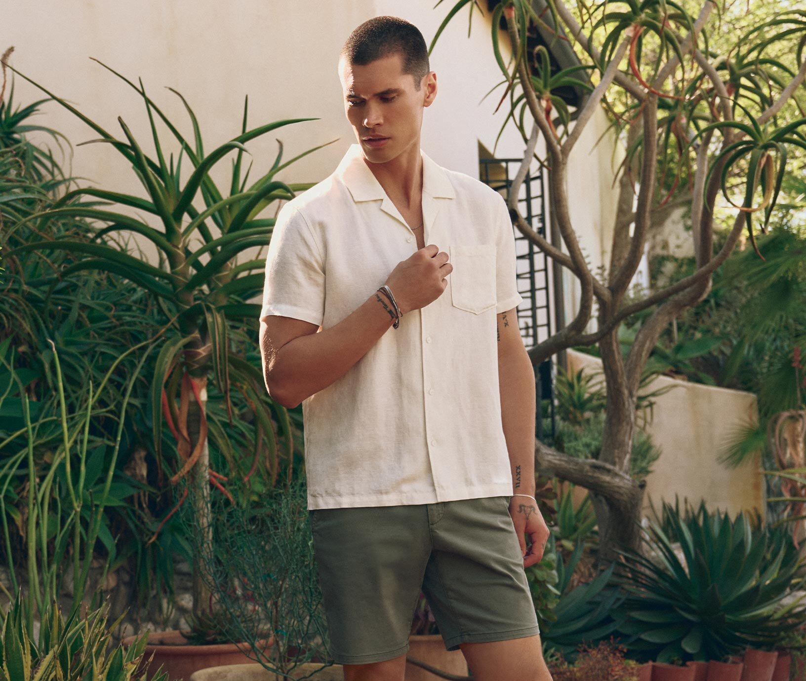 Man wearing an ivory short sleeve button down shirt and green shorts 