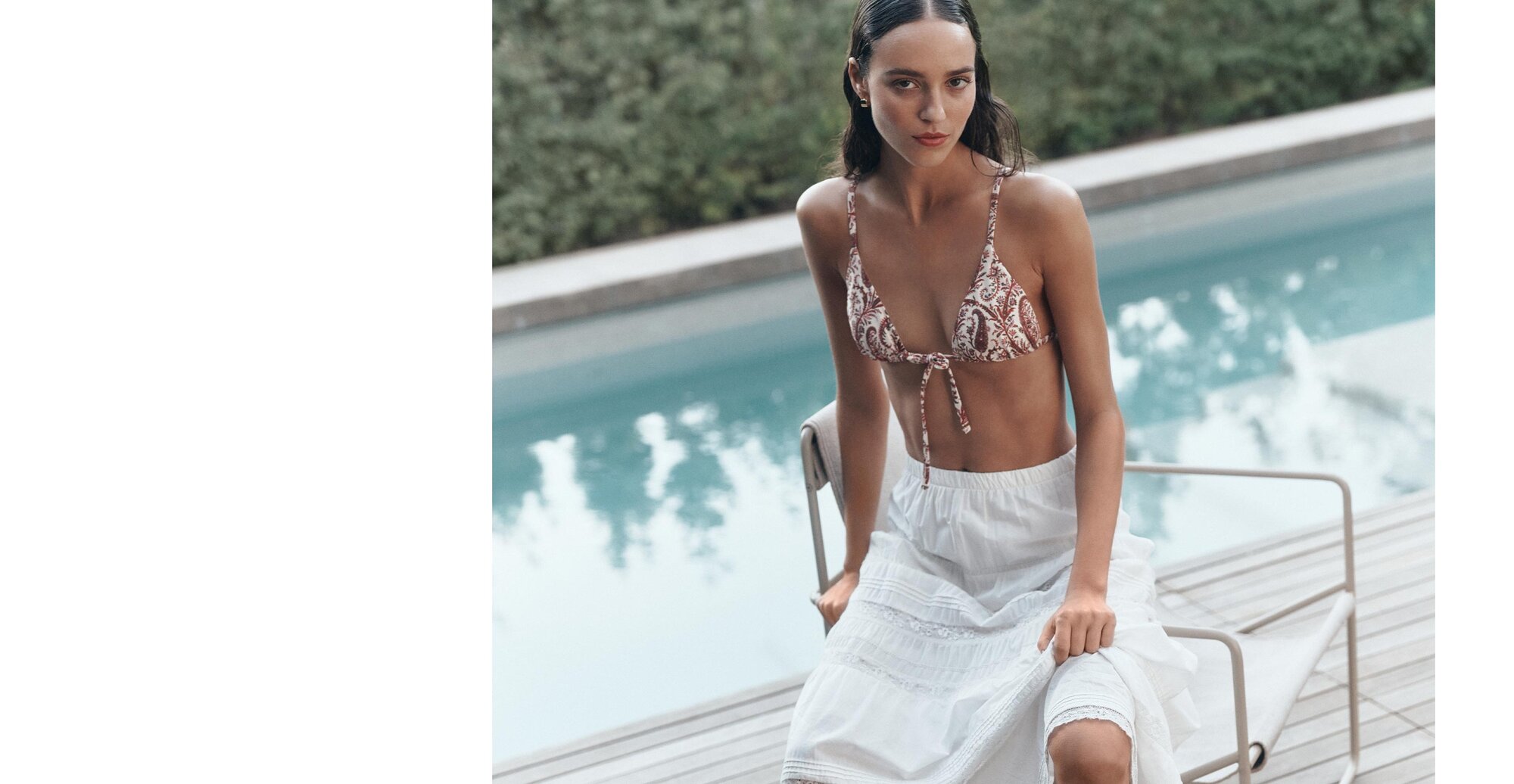 Woman sitting poolside on a chair wearing a paisley print triangle bikini with tie details.