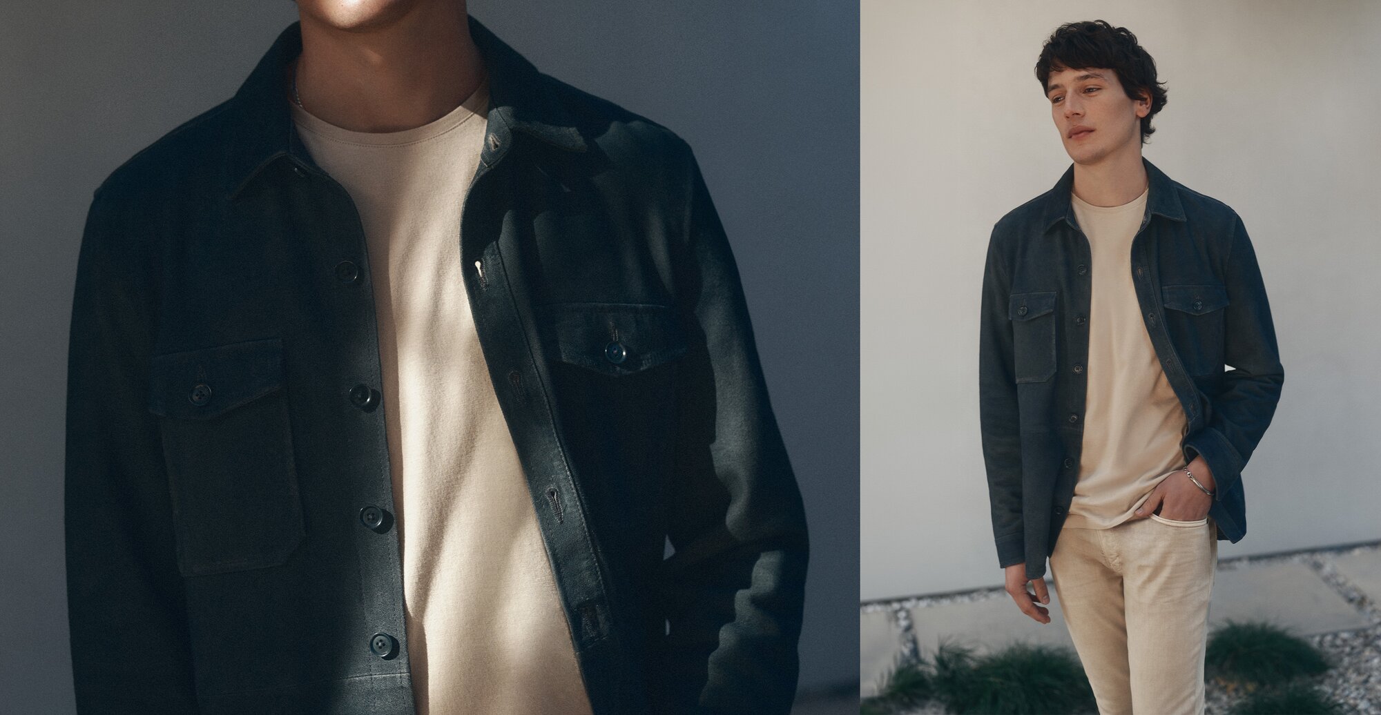 A man standing outside with his hand in his pocket wearing a navy blue suede jacket, a tan t-shirt, and tan denim jeans. 