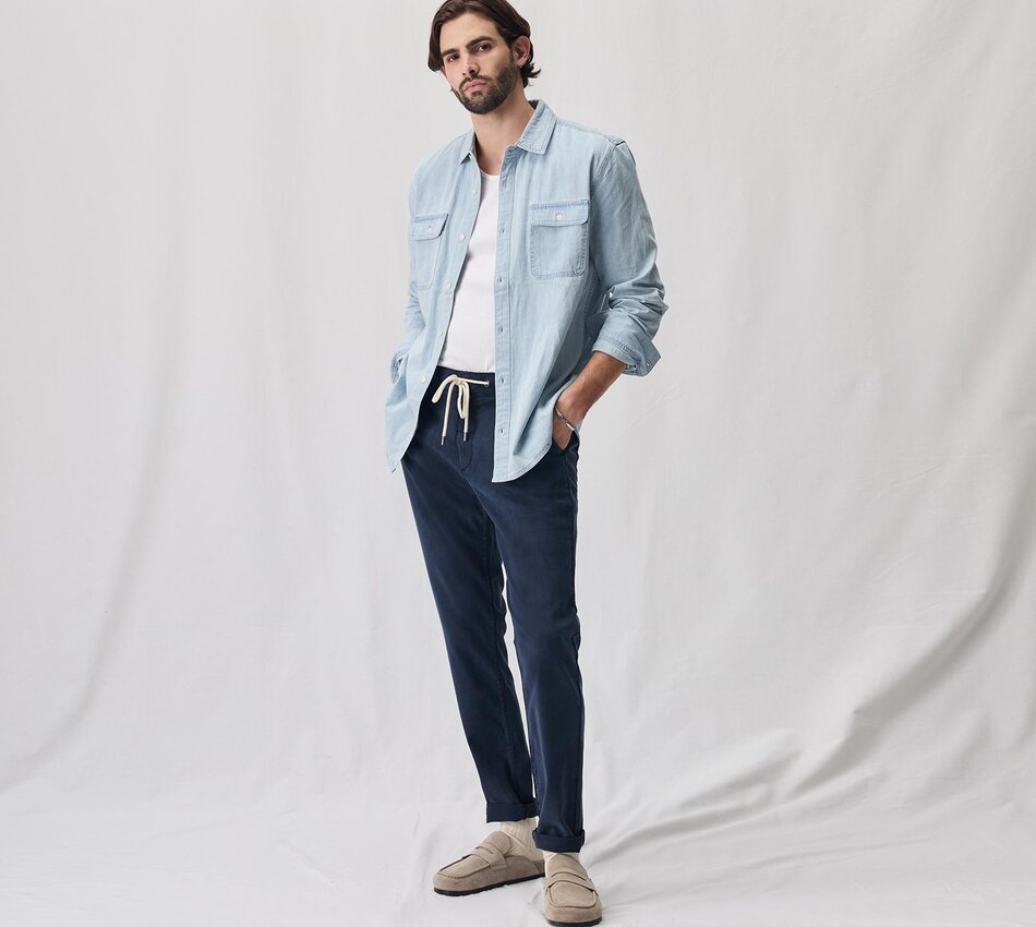 Man wearing a light wash denim button up shirt over a white tank and navy blue jogger pants