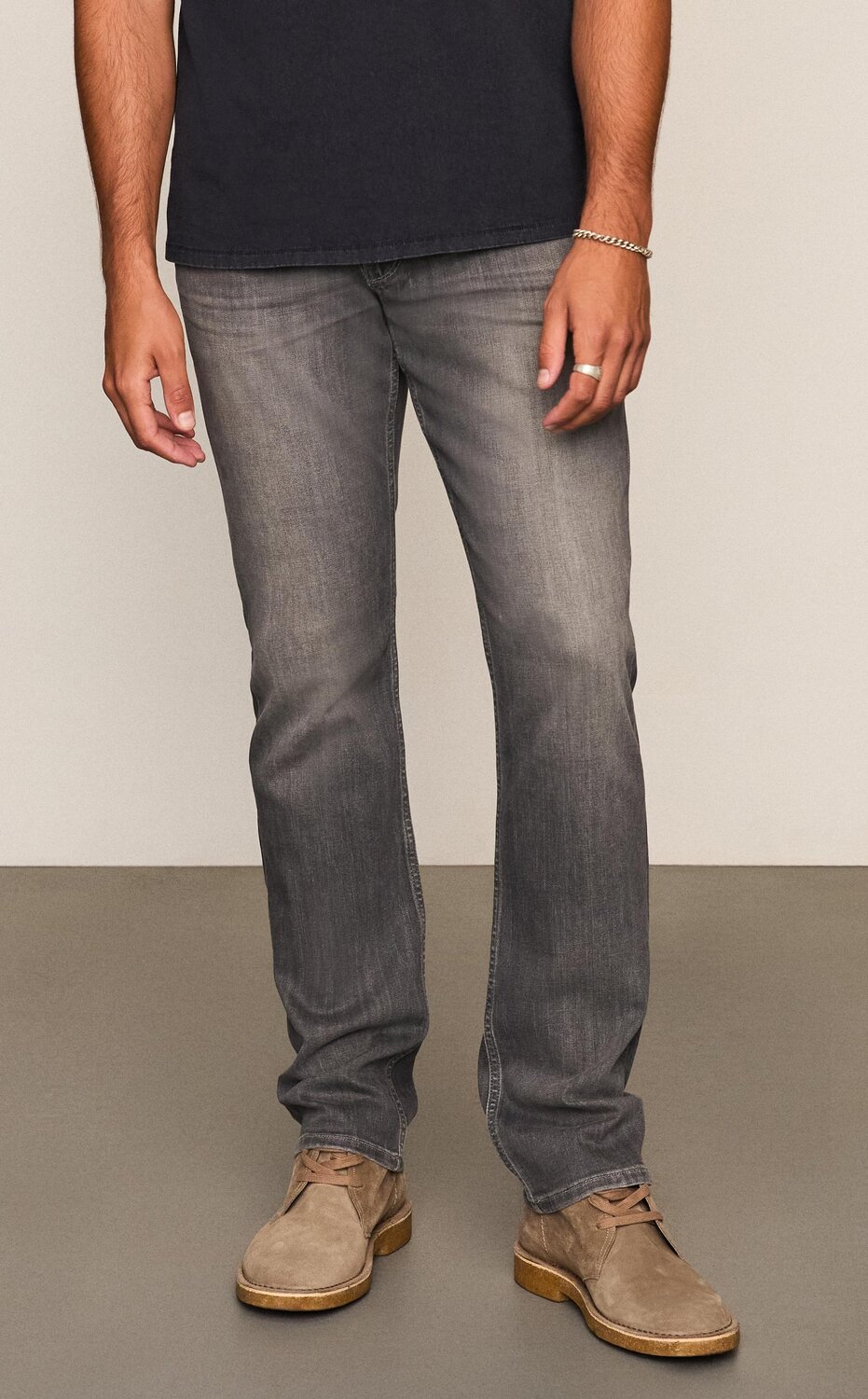 Man wearing a black tee, grey wash jeans and taupe boots