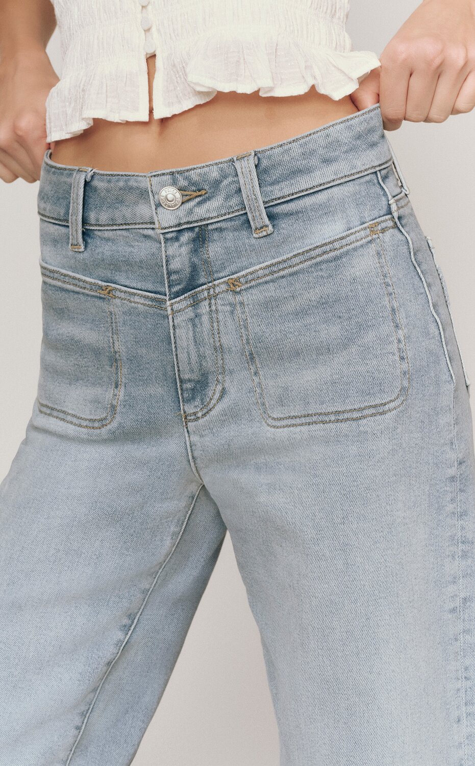 Woman wearing light wash high rise jeans in front of a grey backdrop.