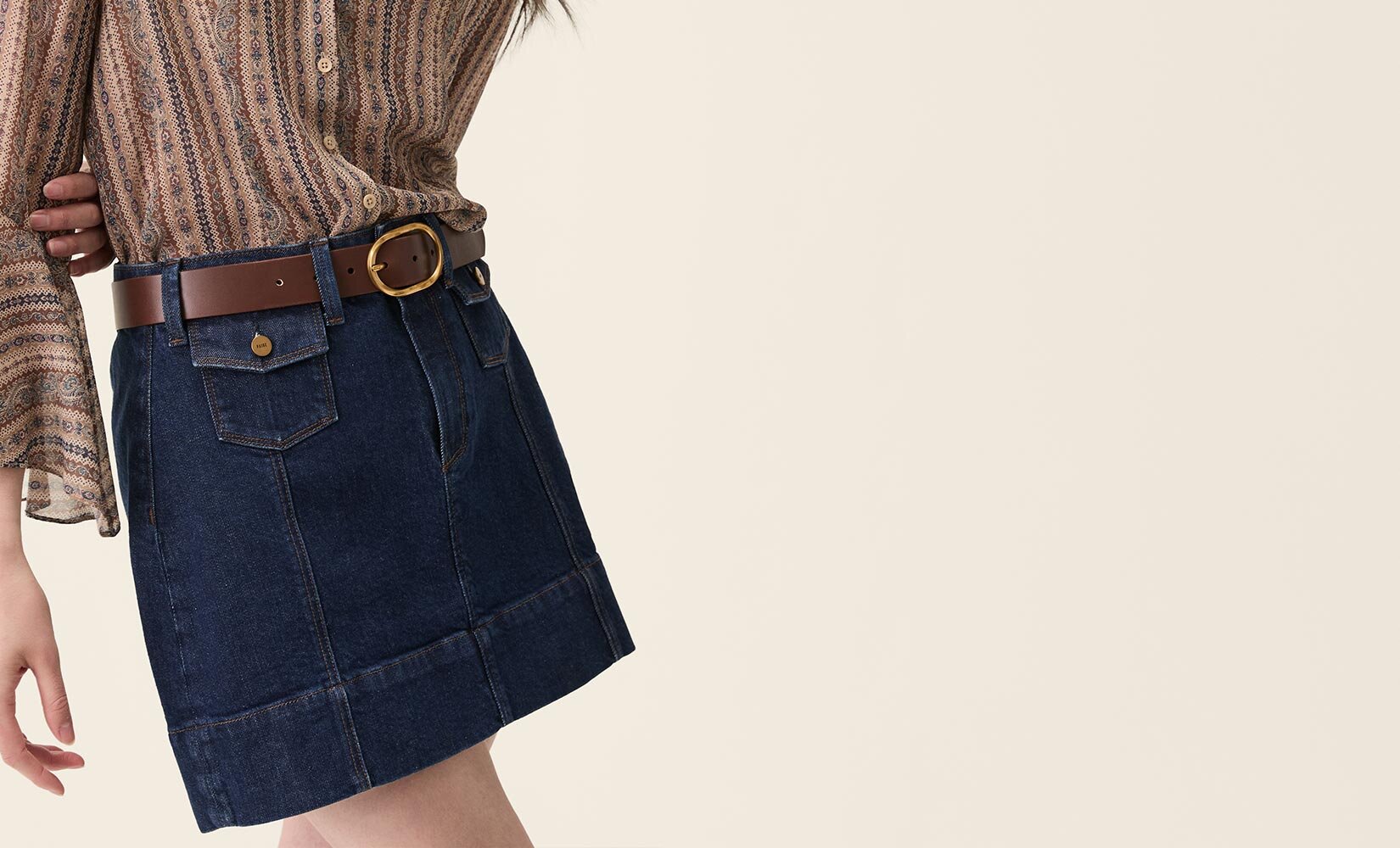 Woman wearing a brown paisley printed blouse, dark wash mini skirt, and brown belt