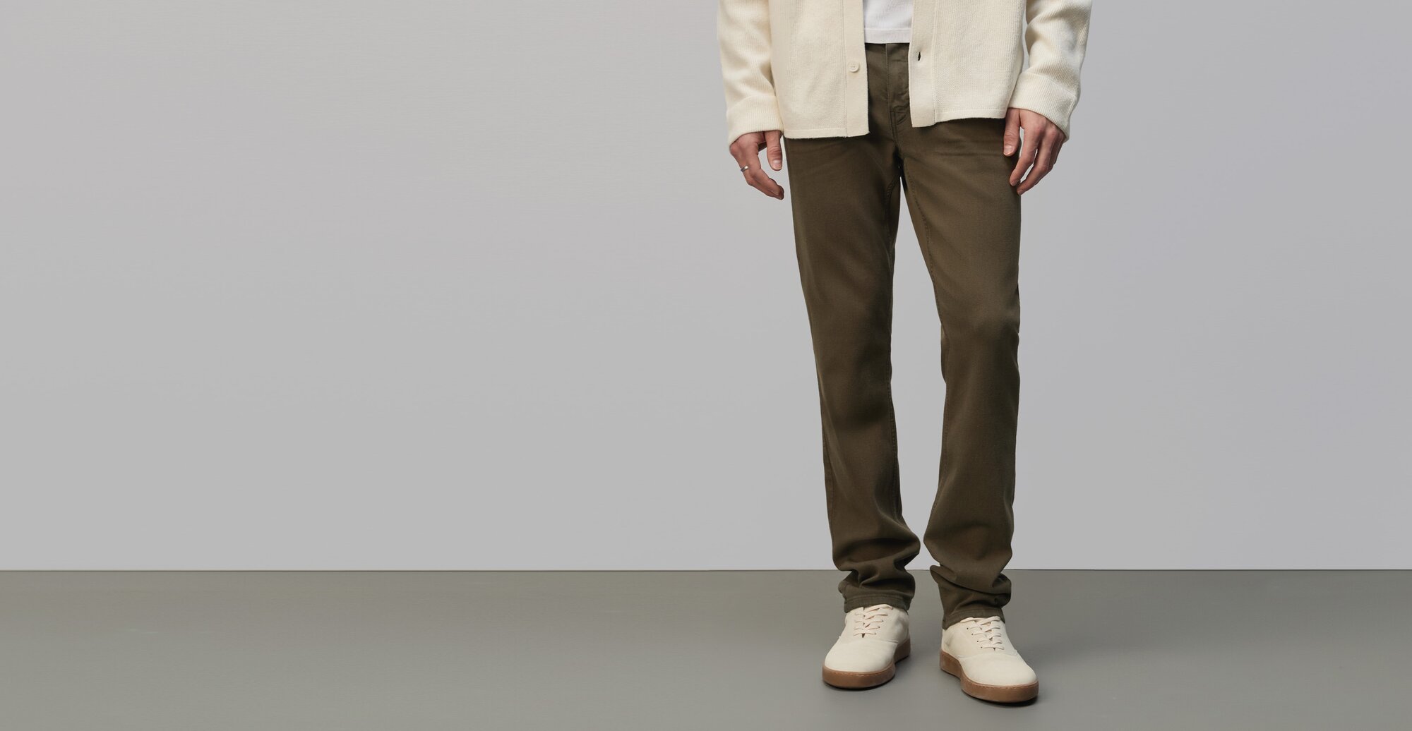 Man wearing a cream cardigan over a white tee, dark olive green jeans, and cream sneakers