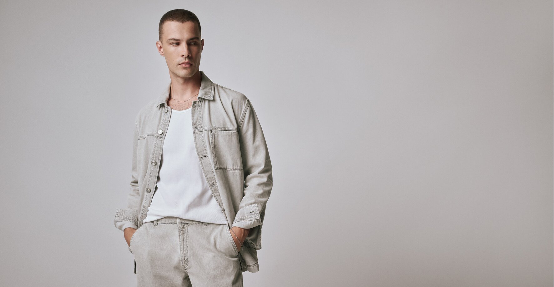 Man wearing a washed light grey denim overshirt with matching denim trousers and a white tank top