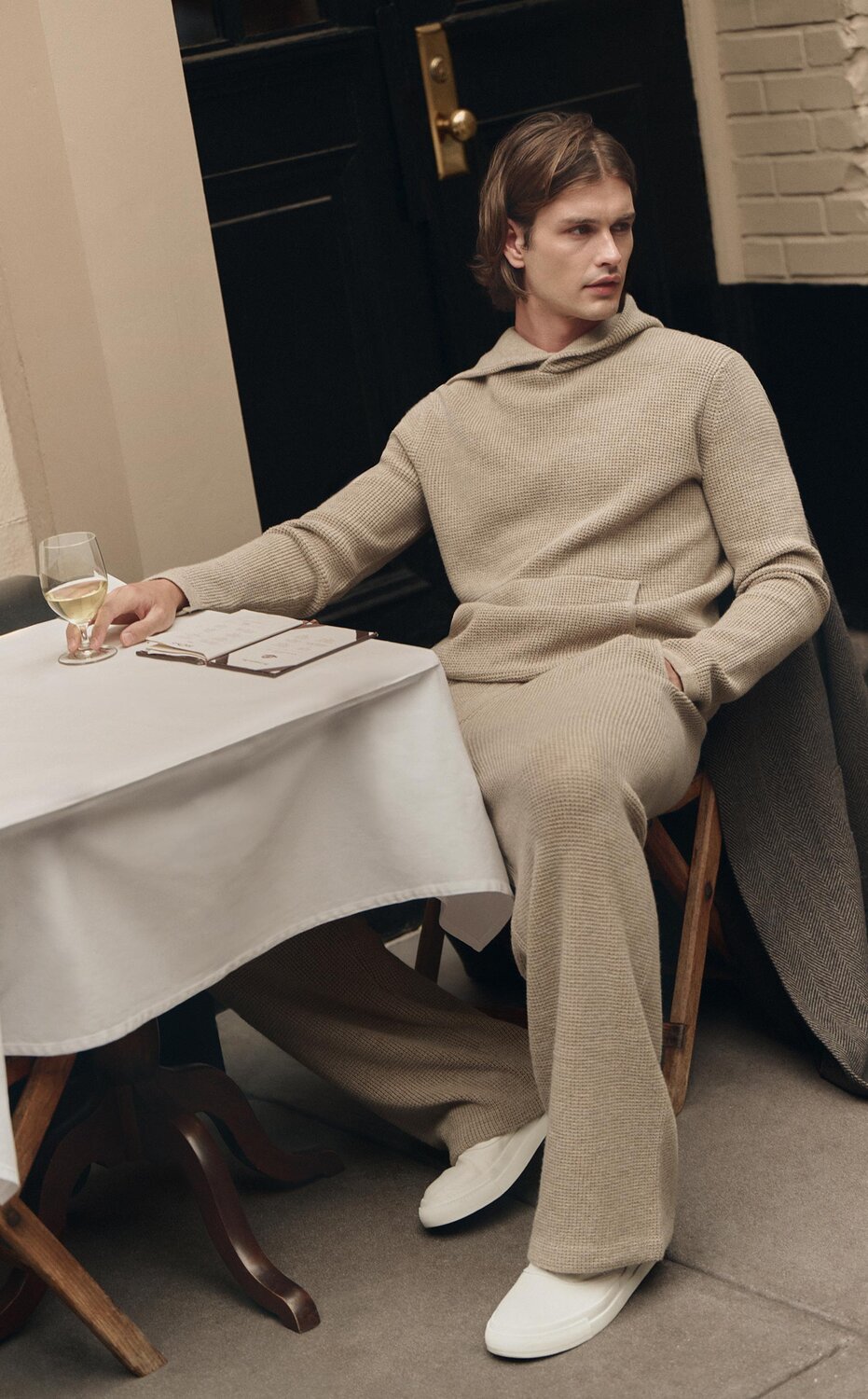 Man wearing a beige sweater knit hoodie and pant set with white sneakers