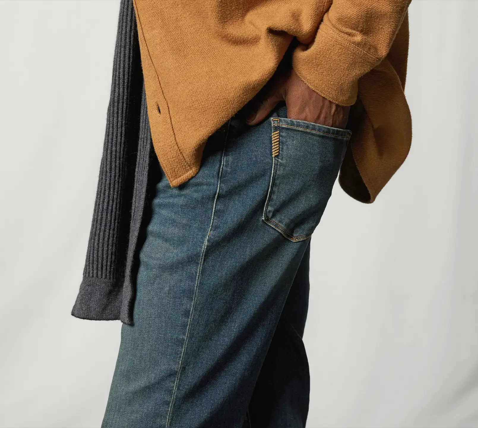 Man standing wearing a light brown overshirt, grey scarf, and dark wash jeans