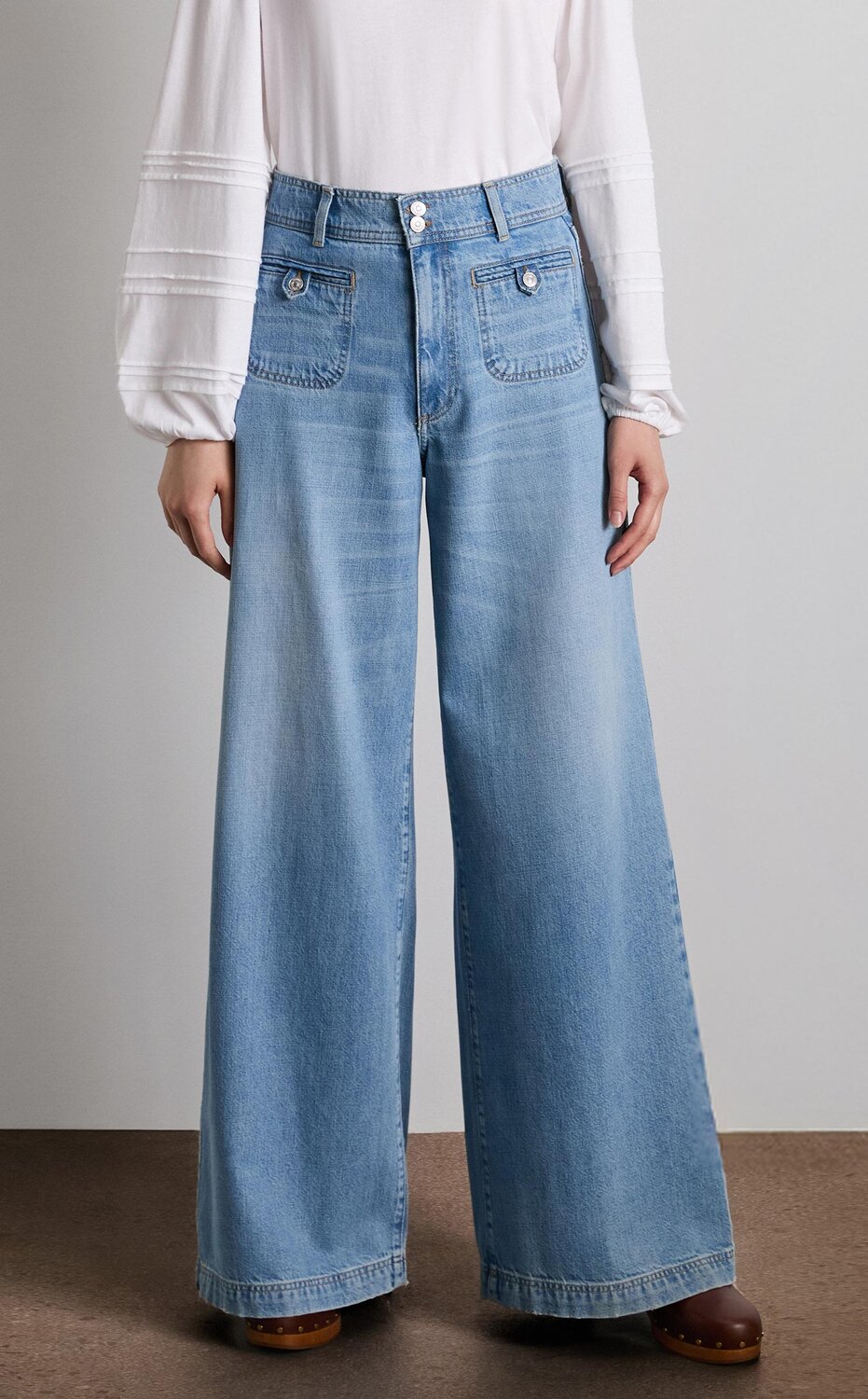 Woman wearing a long sleeve white top tucked into light wash wide leg jeans and auburn clogs