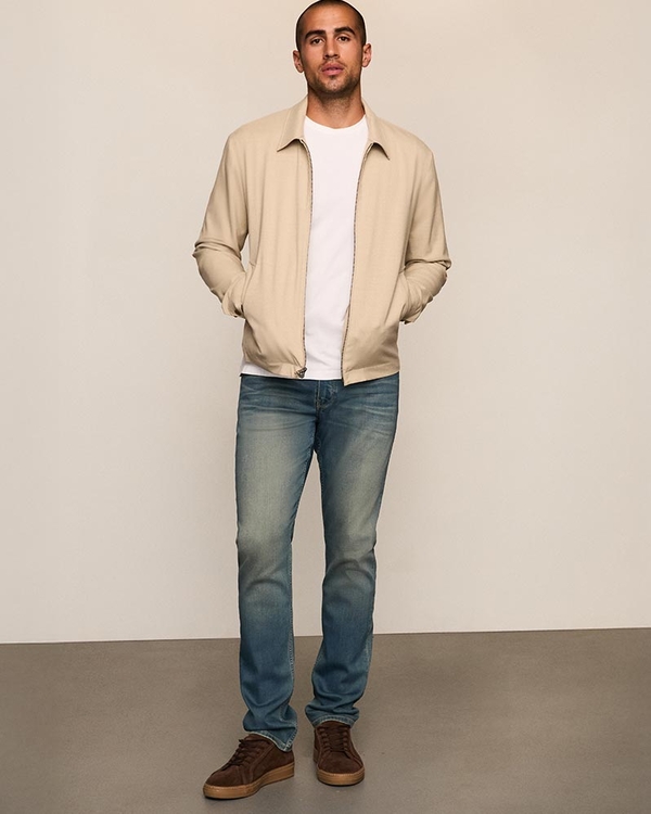 Man wearing a cream jacket over a white tee, dark wash jeans, and brown sneakers