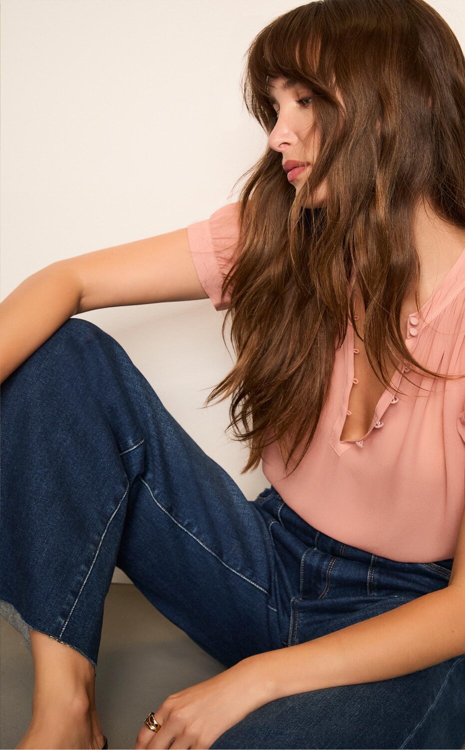 Woman wearing a pink short sleeve blouse, dark wash jeans, and black flats