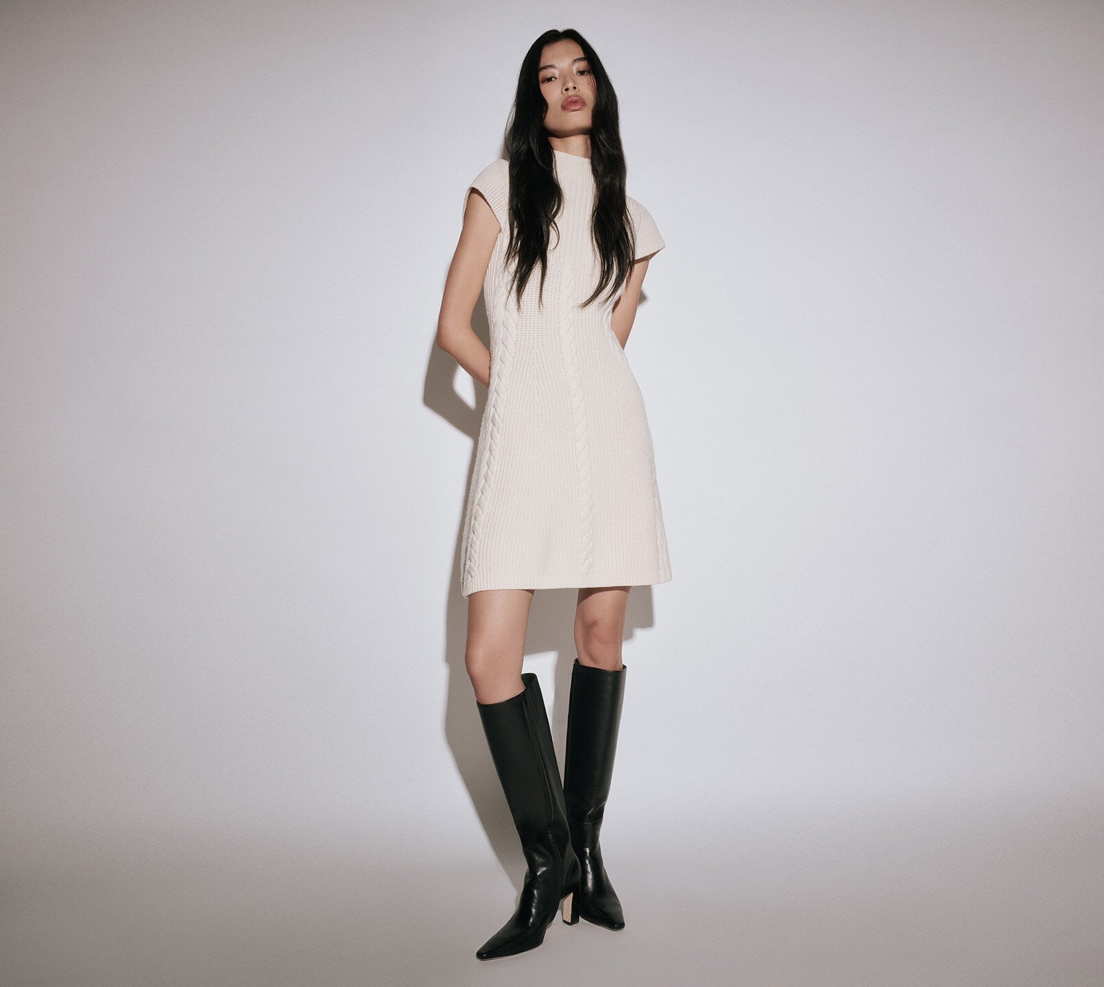 Woman wearing a cream sweater dress with tall black boots