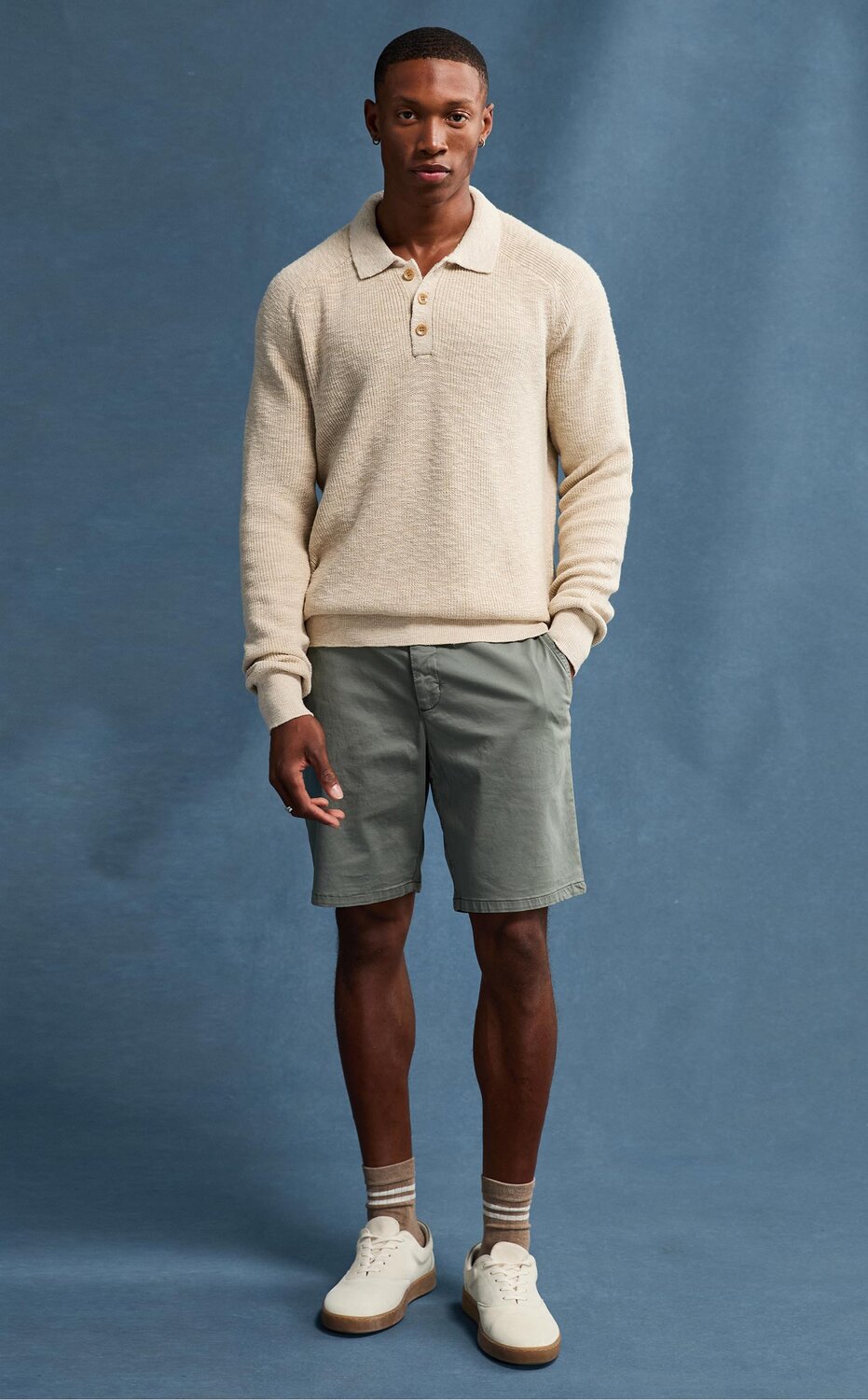 Man wearing a cream sweater polo, green shorts and bone sneakers, man wearing a green jacket over an ivory polo
