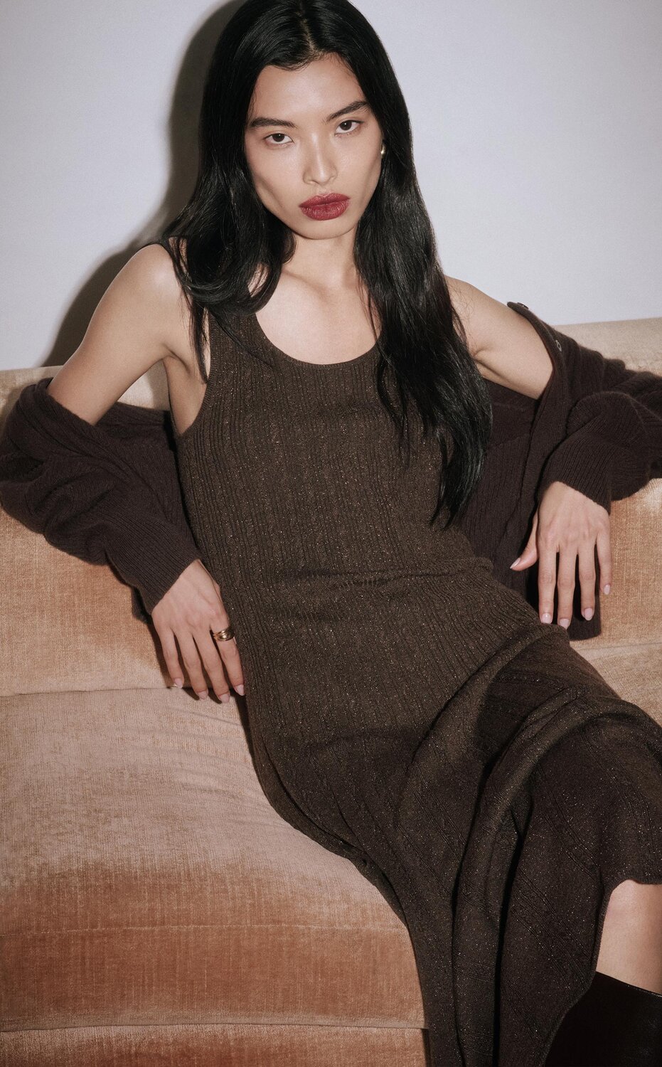 Woman sitting on a couch wearing a long brown sparkle dress with a brown cardigan and tall brown boots