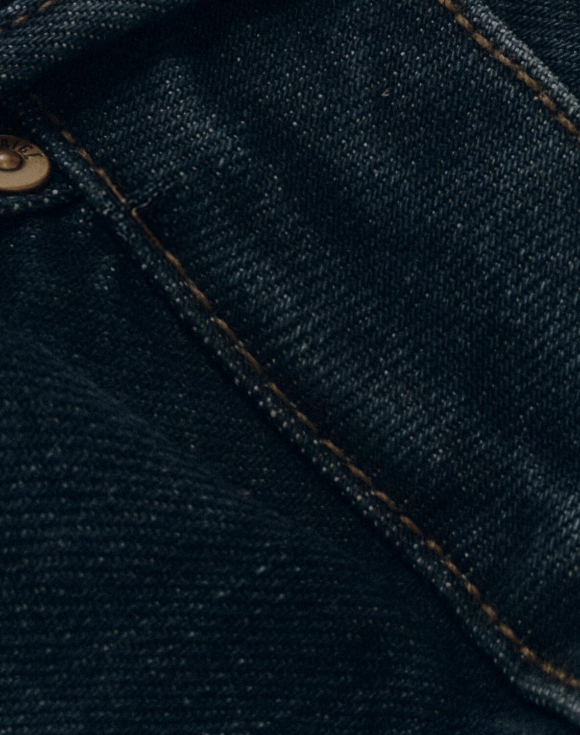 Close-up of denim in a dark blue wash, highlighting pocket and rivet details.
