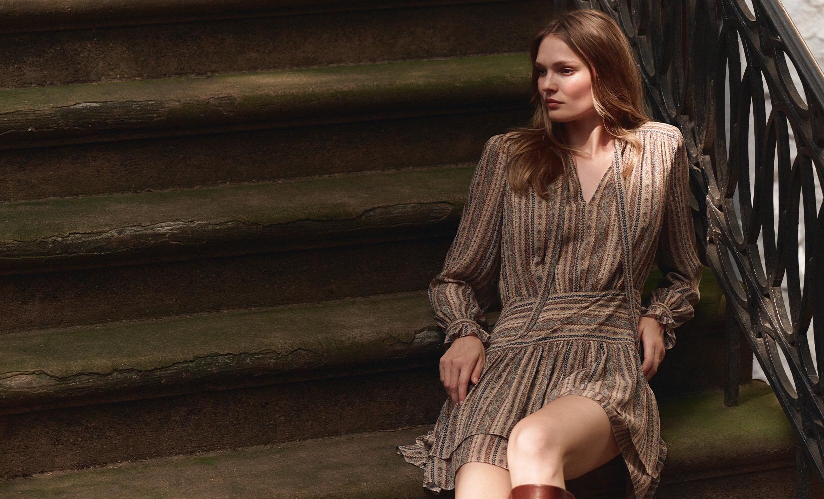 Woman sitting on stairs wearing a long sleeve brown tapestry striped silk mini dress