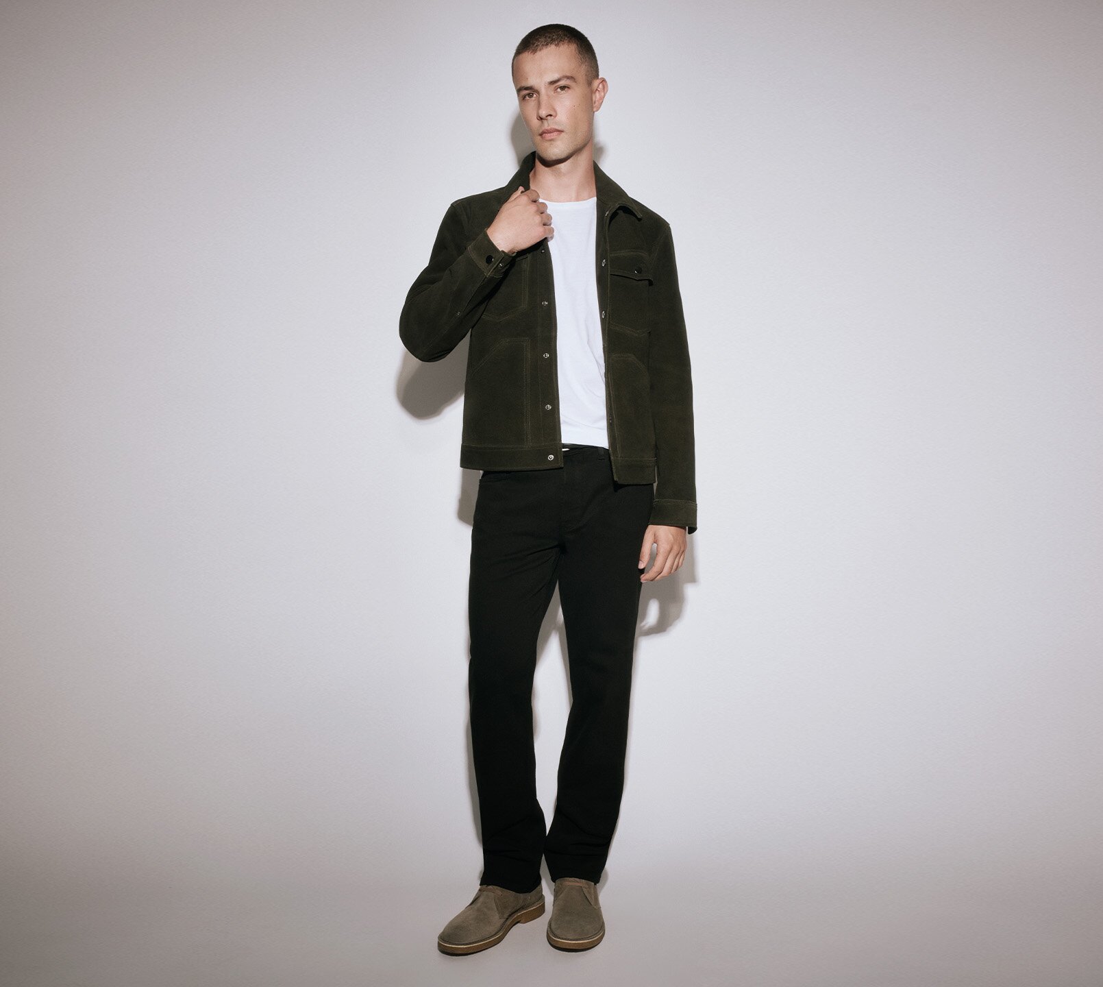 Man wearing a green jacket over a white tee, black jeans, and grey boots