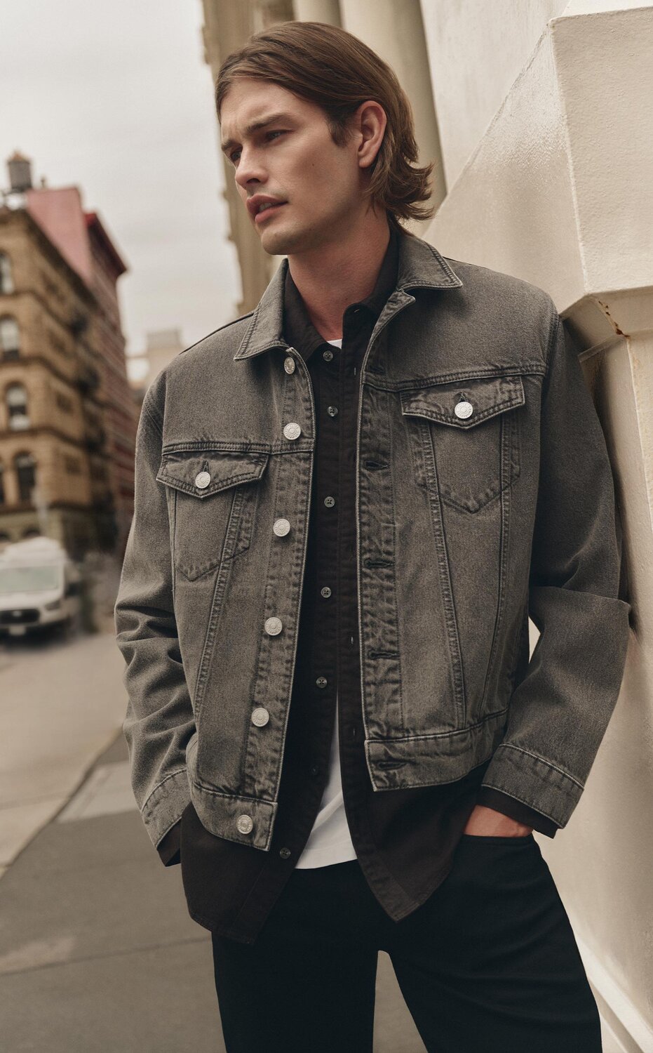 Man wearing a dusty brown wash denim jacket over a dark brown button up shirt, white tee, and dark wash jeans