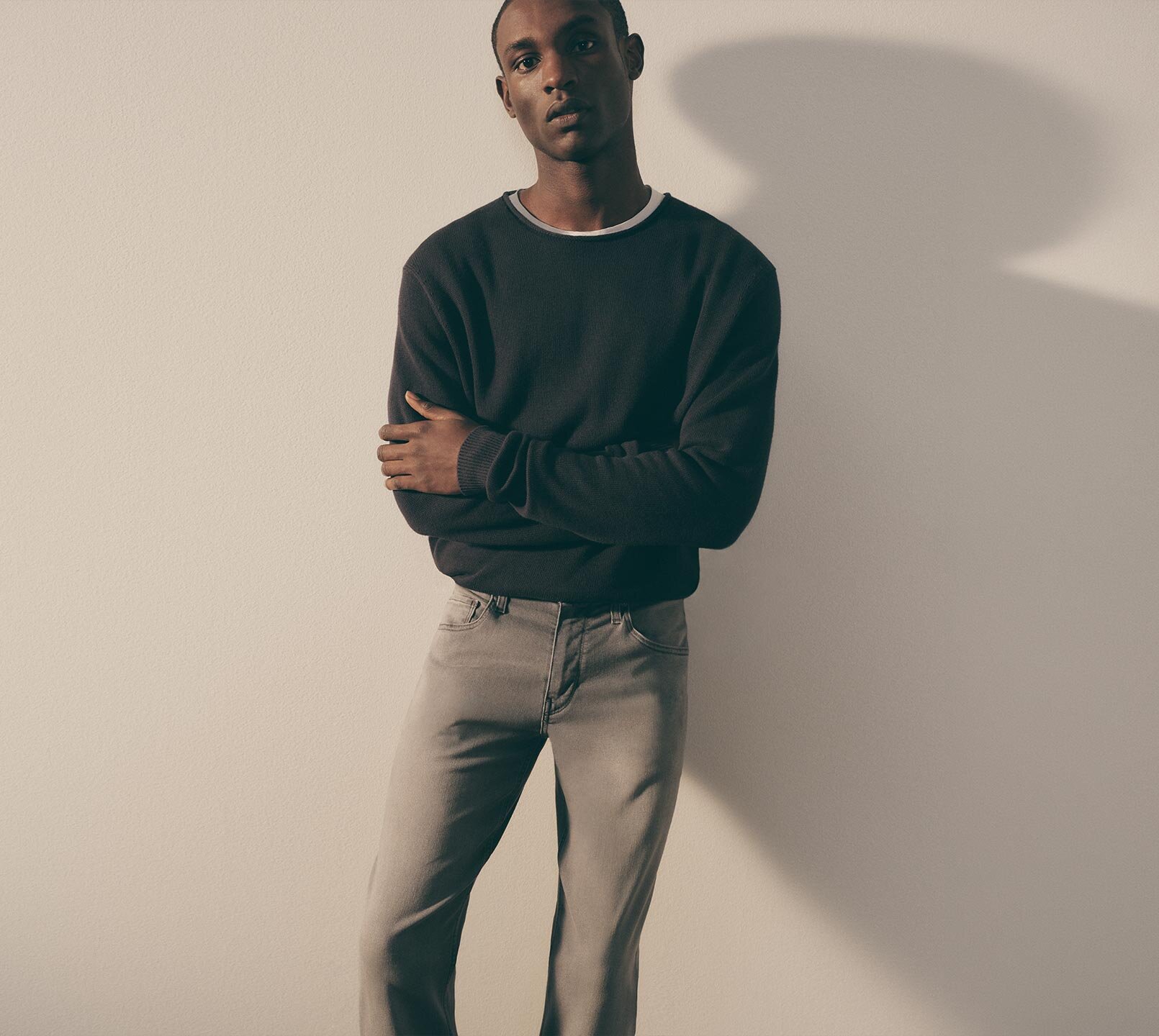 Man wearing a dark navy cotton sweater with roll neck detail, white t-shirt and grey denim jeans all by PAIGE.