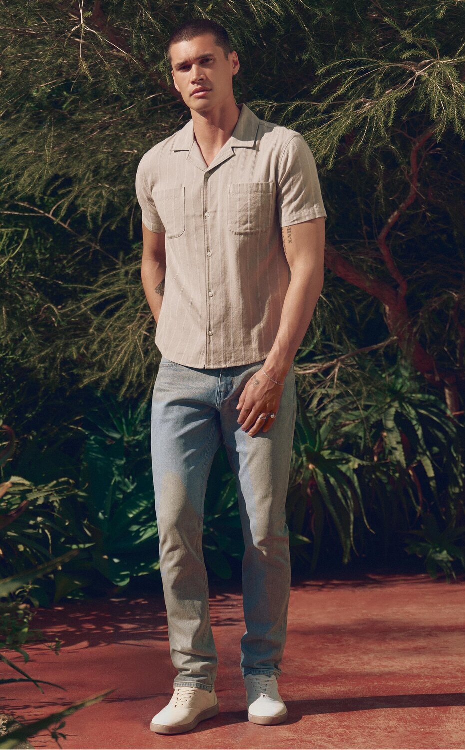 Man wearing a grey striped button up shirt, light wash jeans and bone sneakers