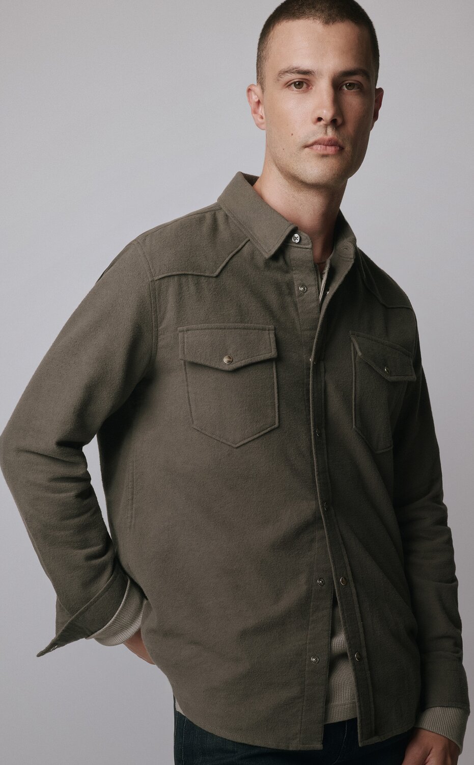 Man wearing a grey button-up shirt over a grey long sleeve tee and dark wash jeans