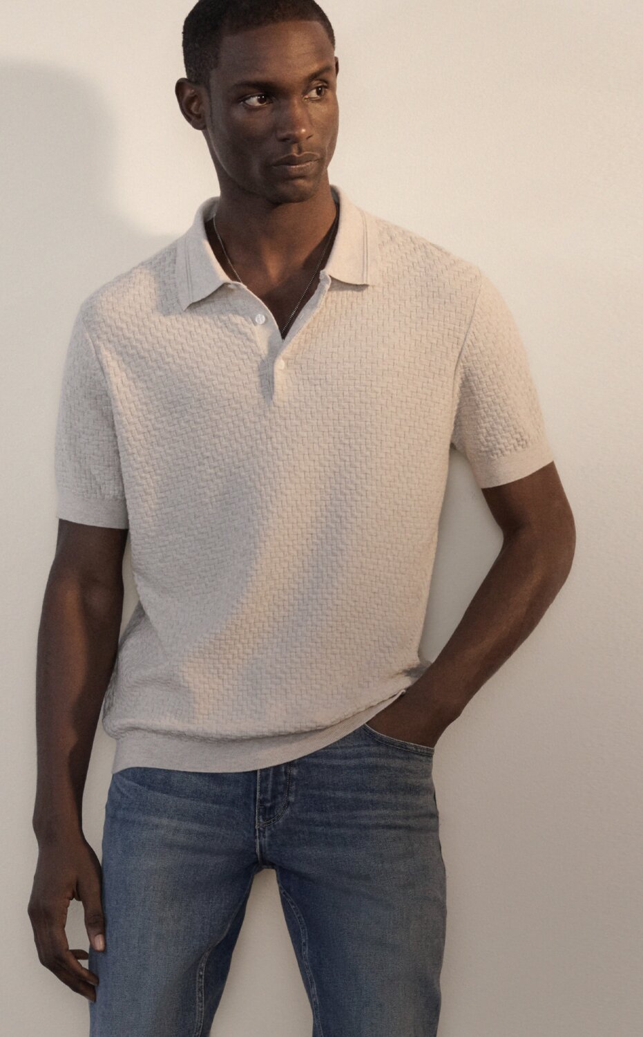 A man wearing a light tan textured short sleeve polo shirt and medium blue denim jeans.