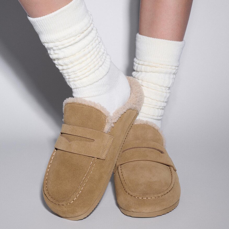 Woman wearing a pair of suede camel shearling slide loafers