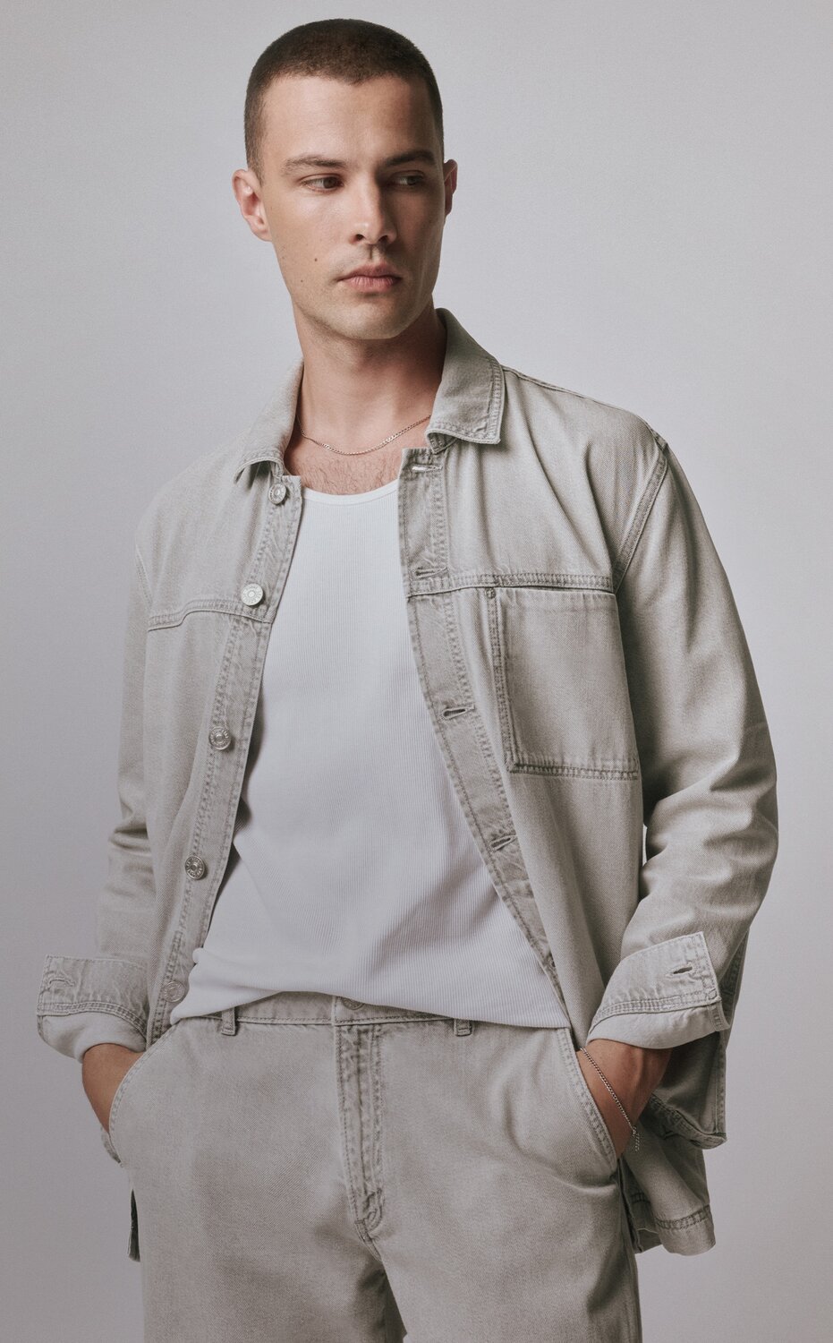 Man sitting in a chair wearing a cream long sleeve sweater polo and pale silver jeans