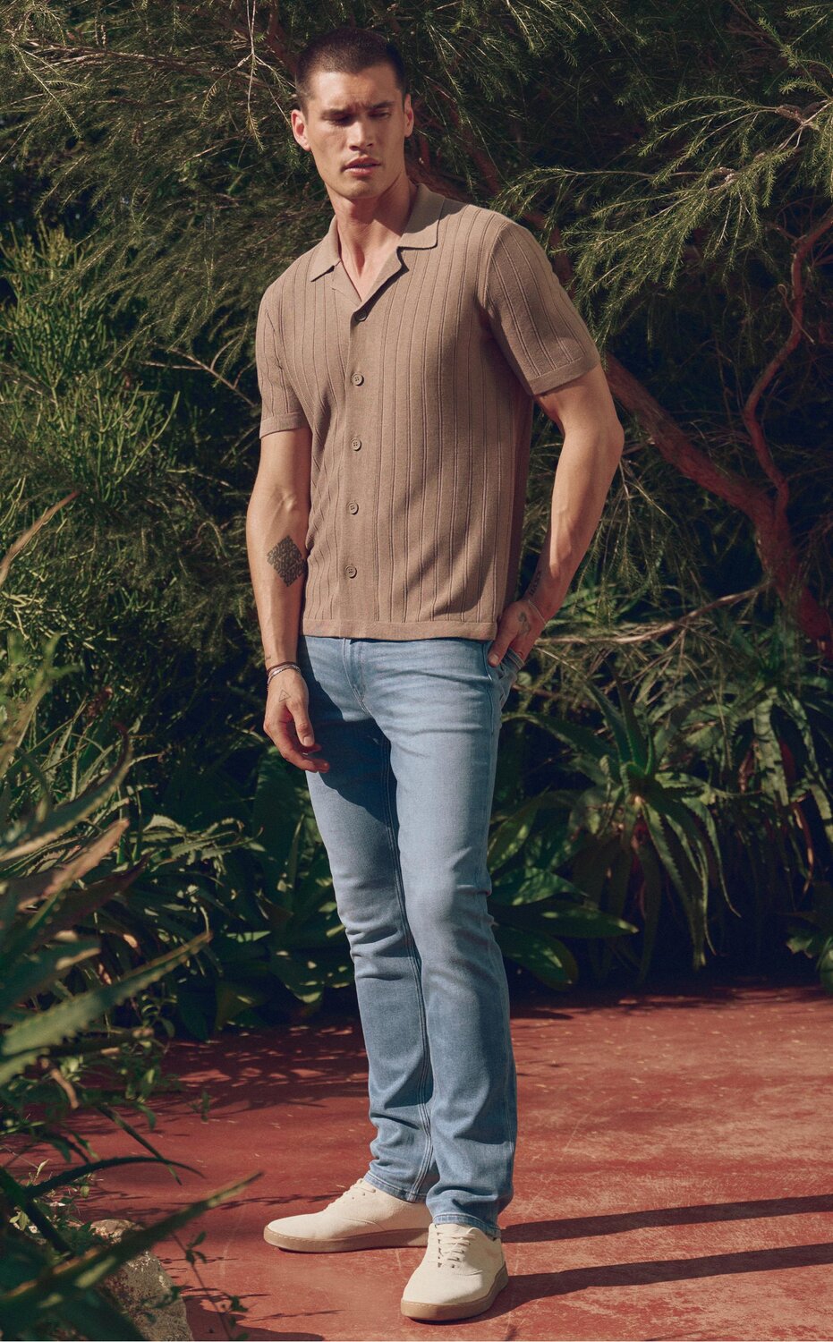 Man wearing a grey striped button up shirt, light wash jeans and bone sneakers