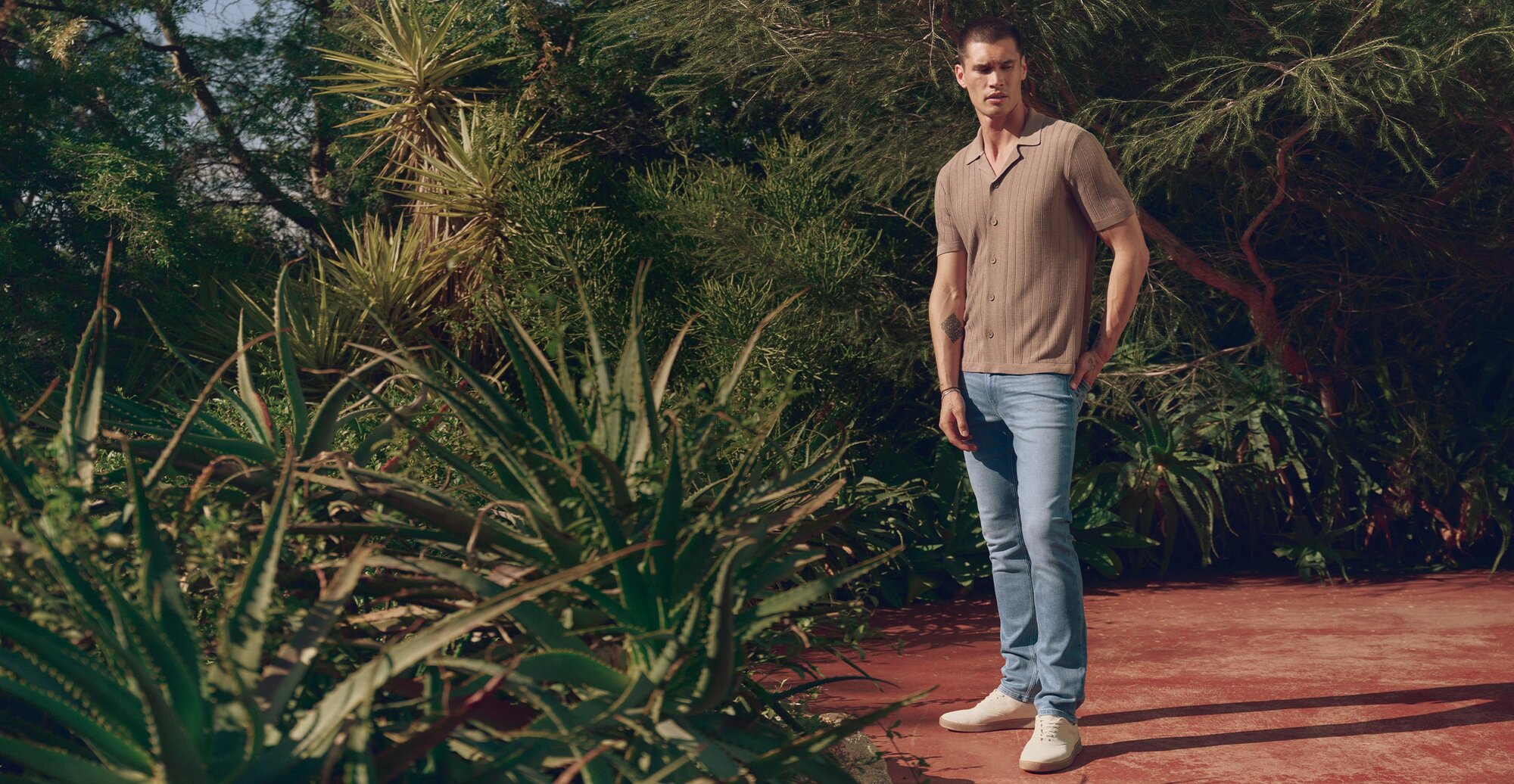 Man wearing a grey striped button up shirt, light wash jeans and bone sneakers
