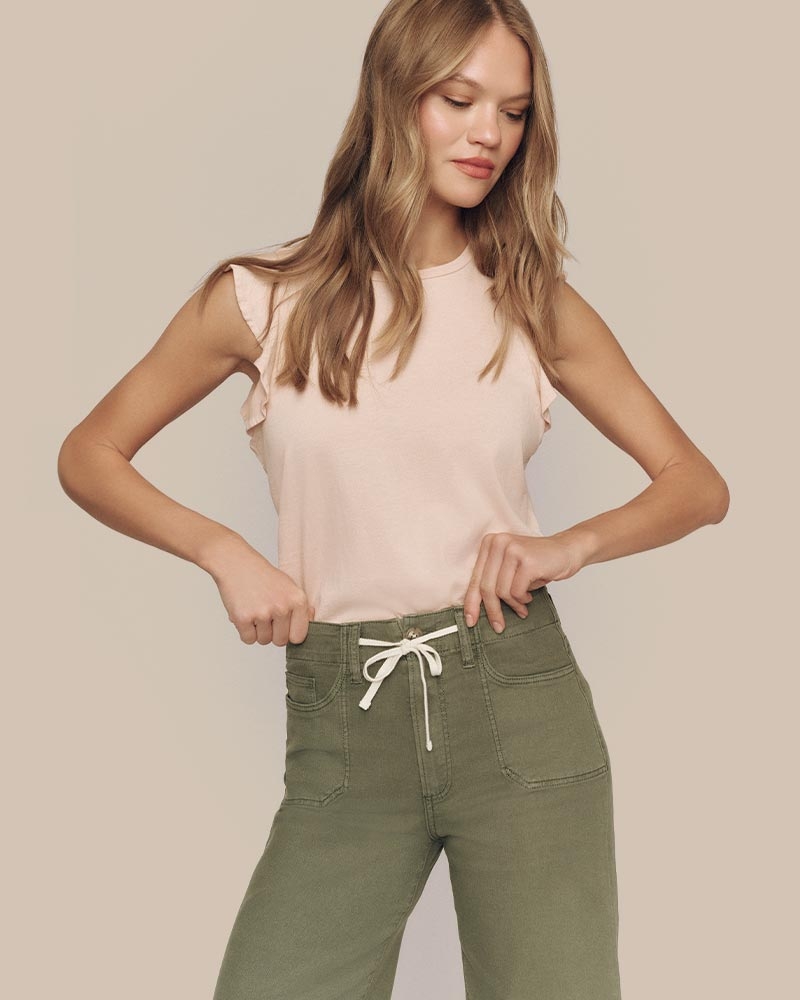 Woman wearing a sleeveless top and green pants with a drawstring waist, adjusting the waistband.