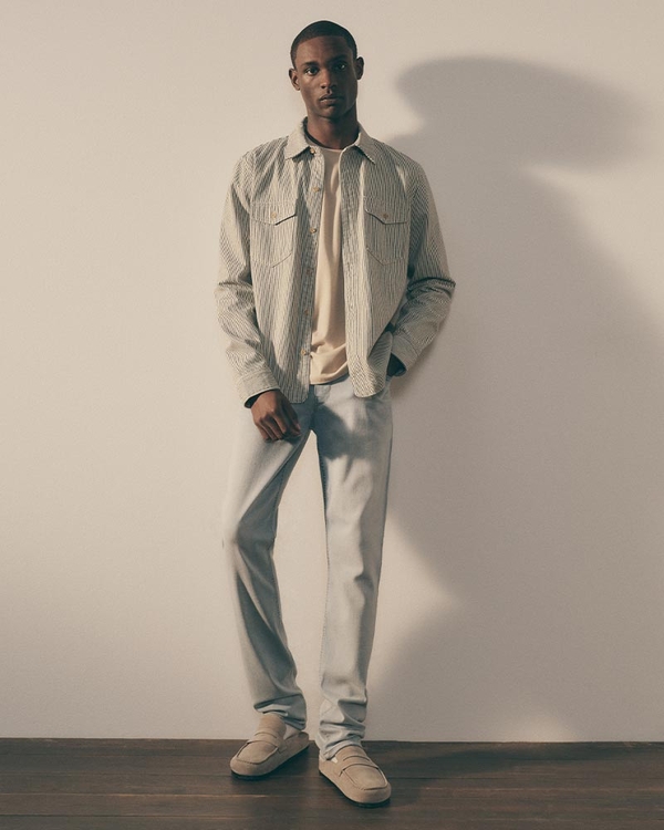 Man wearing a striped button-up shirt and light pants, standing in a studio setting.