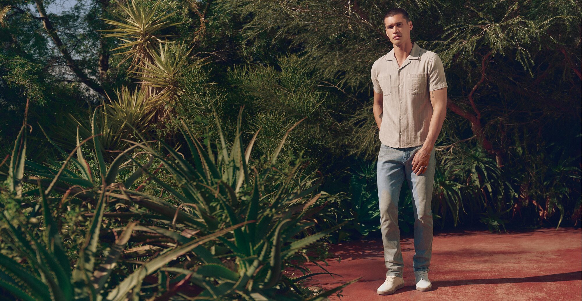 Man wearing a grey striped button up shirt, light wash jeans and bone sneakers
