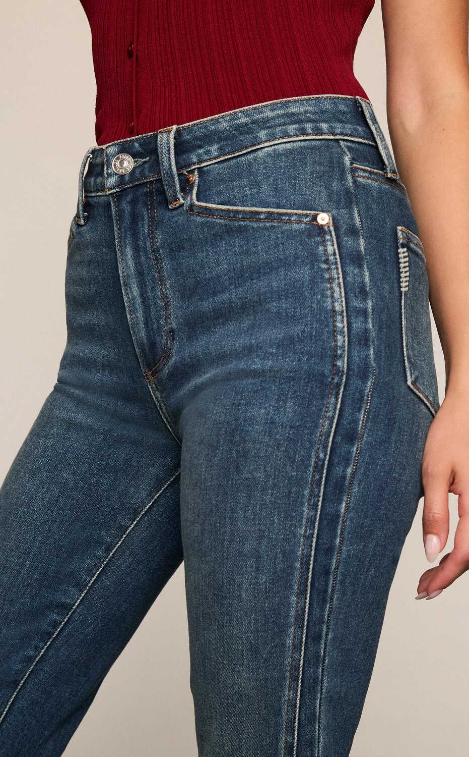 Woman wearing a cranberry sweater tank with dark wash bootcut jeans and a black pointed toe heel